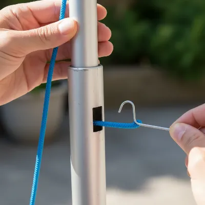 A close-up view of hands using a wire hanger to rethread a new patio umbrella string through the hollow pole.