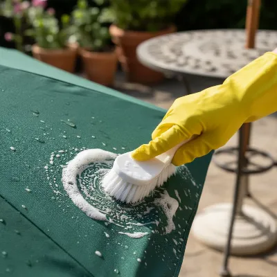 A person wearing gloves using a soft-bristle brush to scrub a moldy patio umbrella with a DIY cleaning solution.